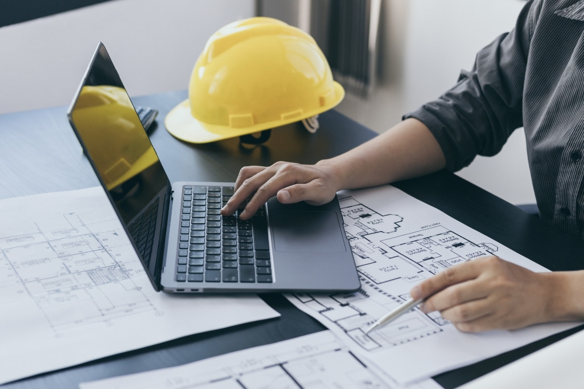 Generálkivitelező építési terveket ellenőriz laptop segítségével, védősisakkal az asztalon