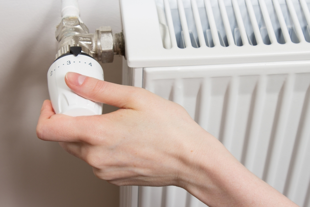 Kéz a radiátor termosztátján, amint a fűtést szabályozza.