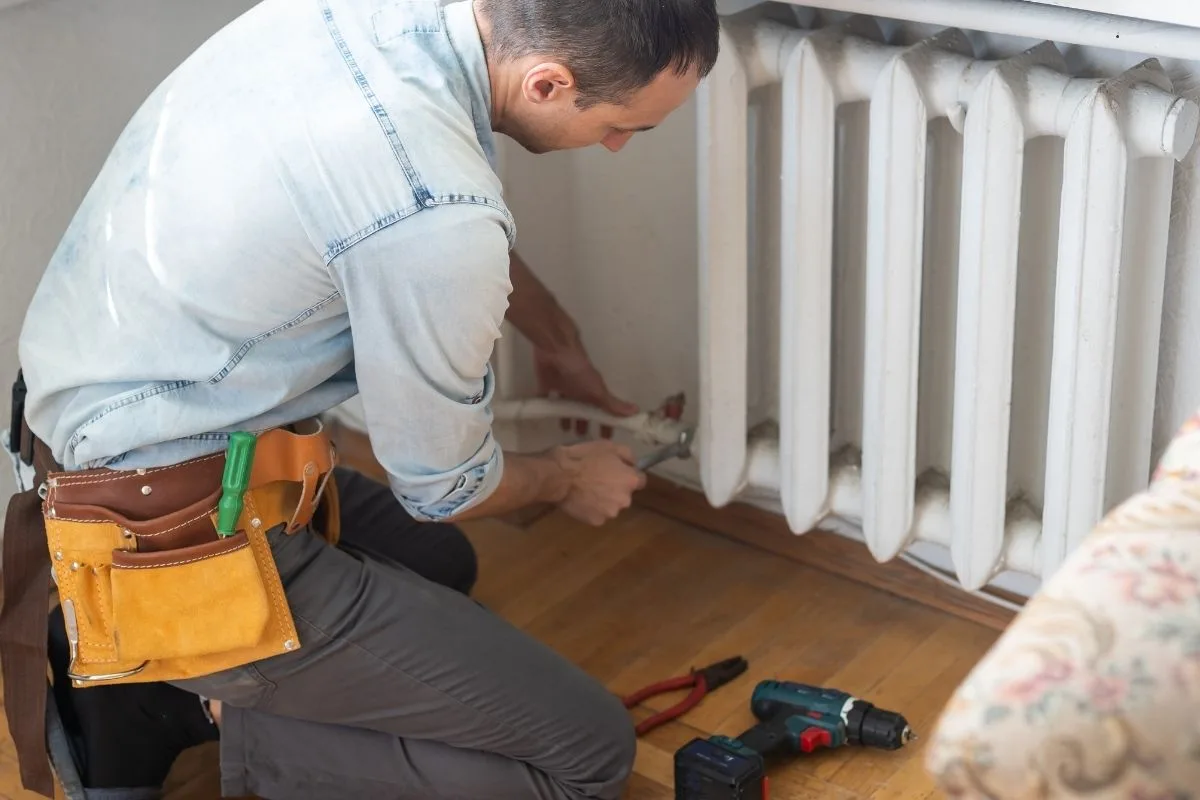 Szerelő radiátor karbantartást végez egy otthonban, szerszámokkal a padlón.